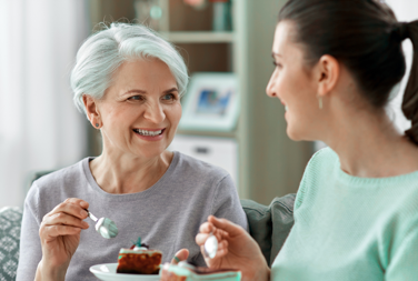 Older Woman And Younger Woman At Home Eating Cake