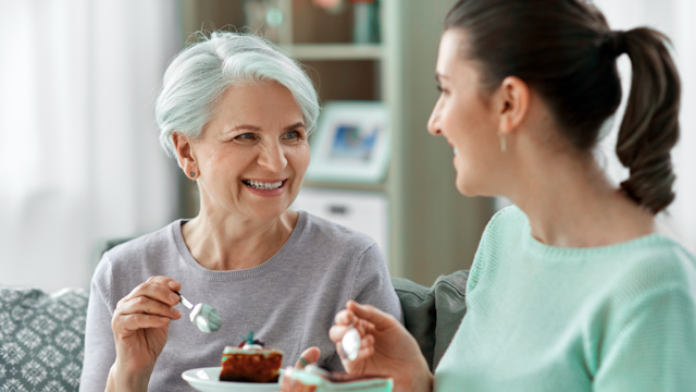 Older Woman And Younger Woman At Home Eating Cake