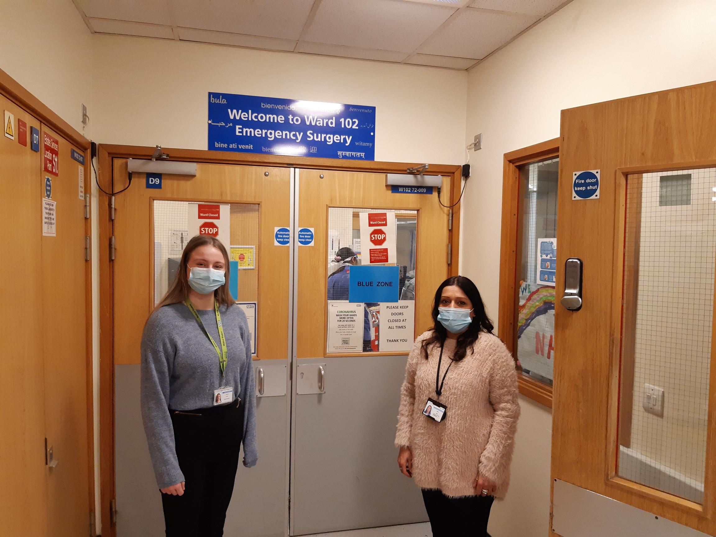 Two women standing outside a hosptial ward with face masks and lanyards on