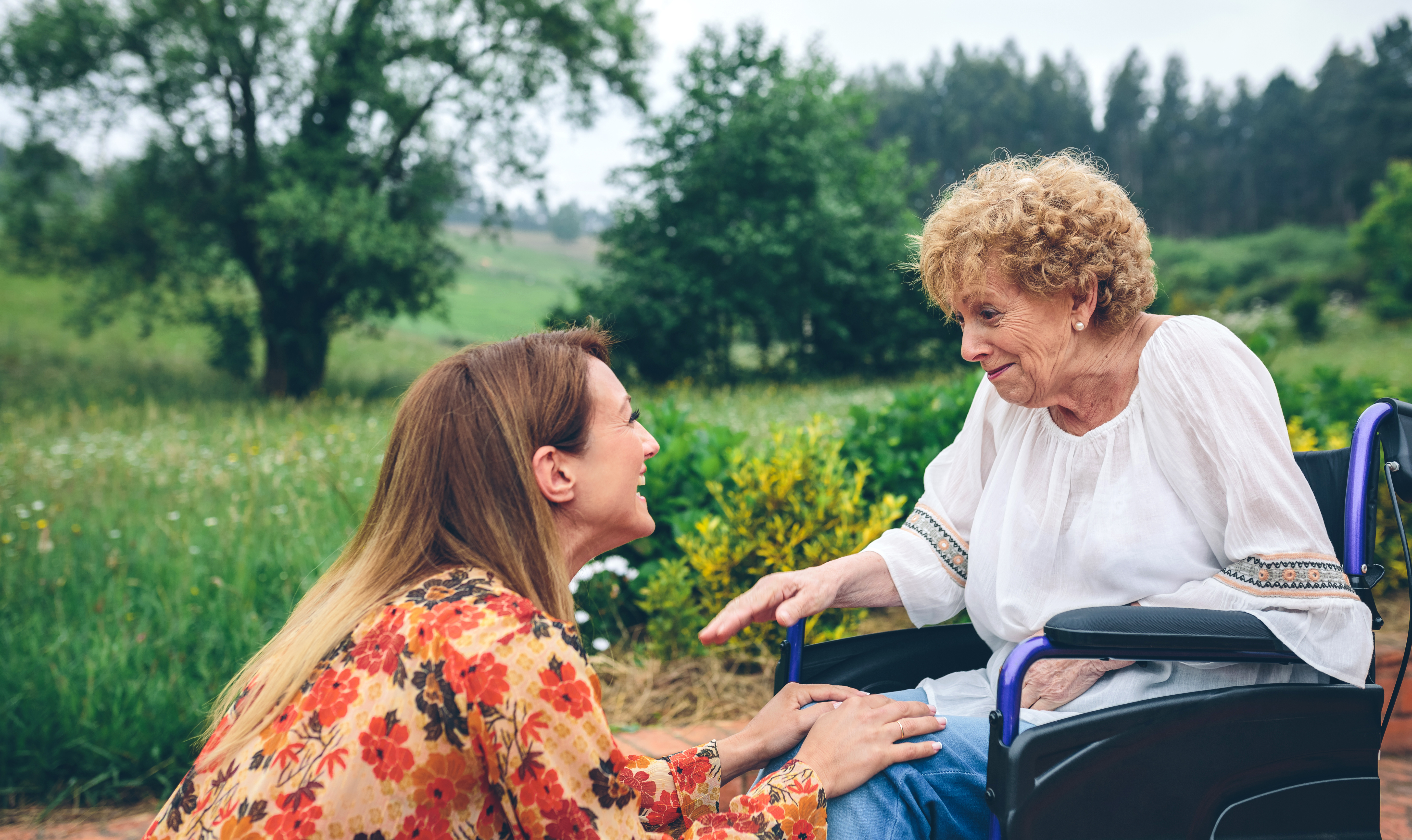 Older woman in a wheelchair being helped by younger woman in the countryside
