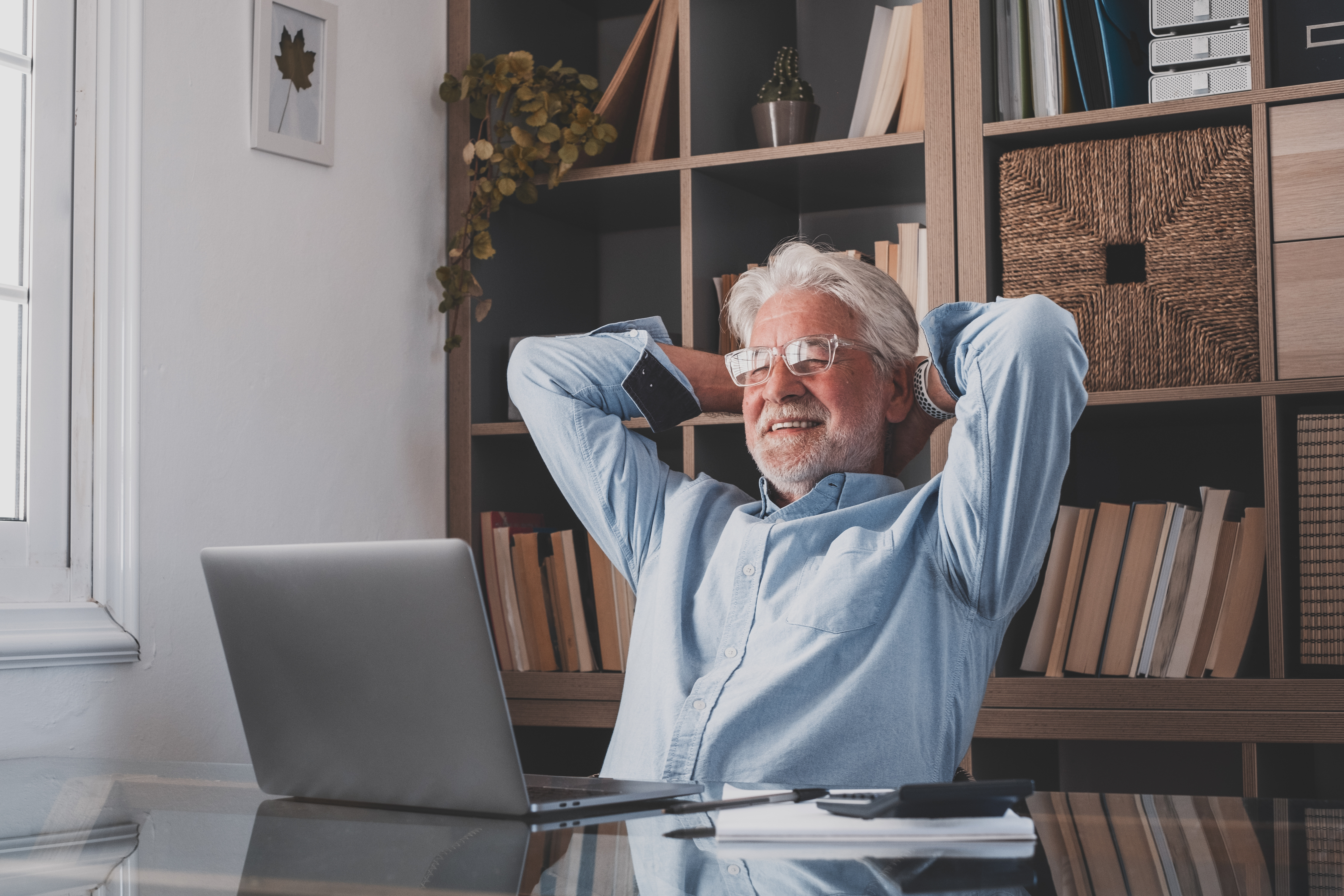Older man sat at a desk looking at his laptop looked relaxed and stress free
