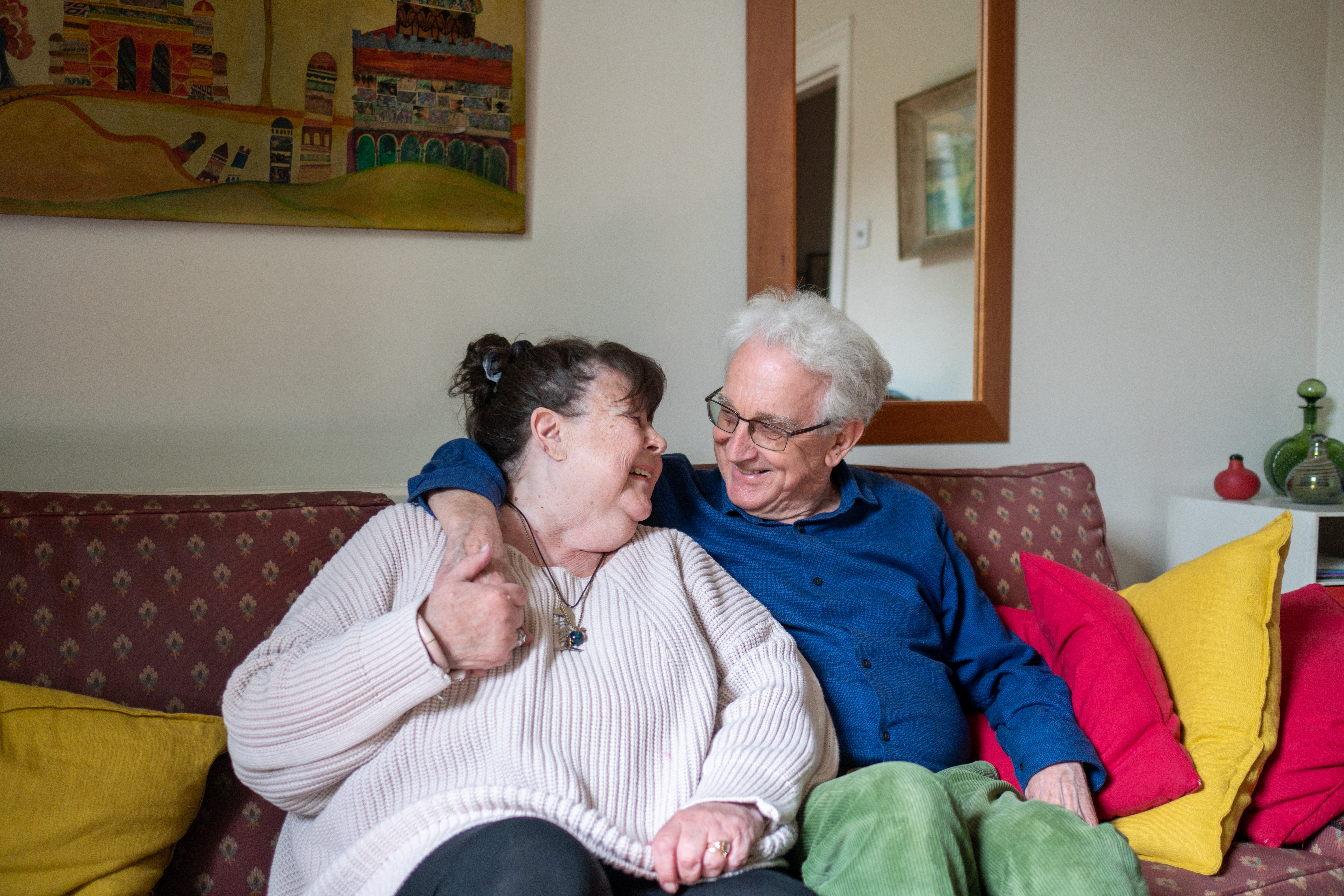 An older couple sat cuddling and smiling to one another on a sofa